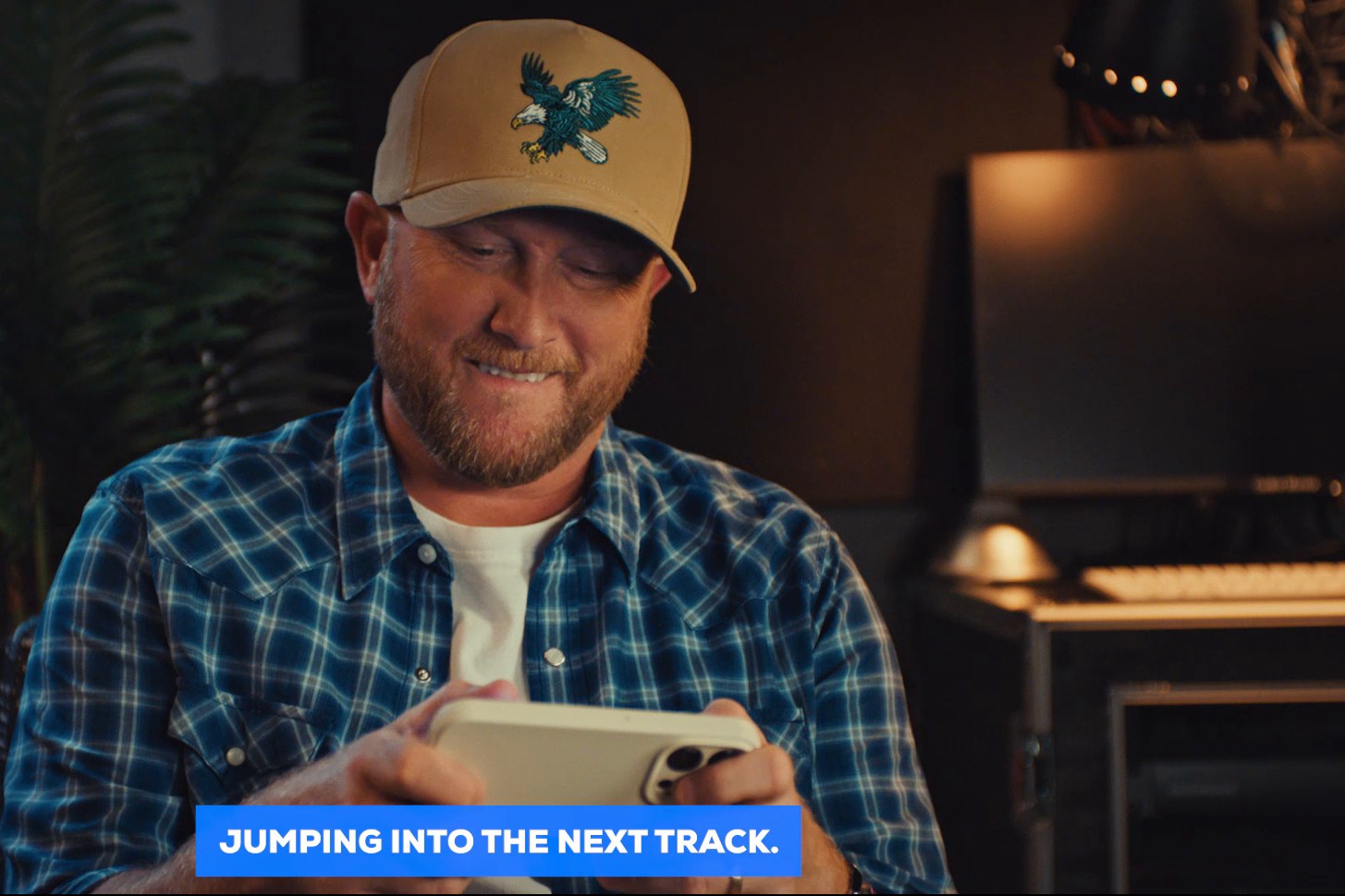 Cole Swindell smiling as he plays on his phone in a warm recording-studio setting