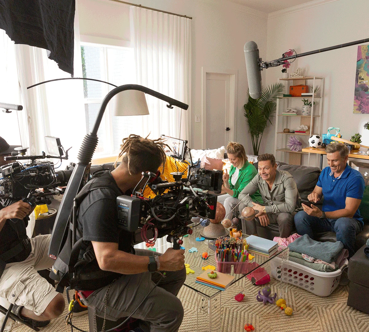 A camera operator filming a sofa scene with Ryan Seacrest and cast in 2024