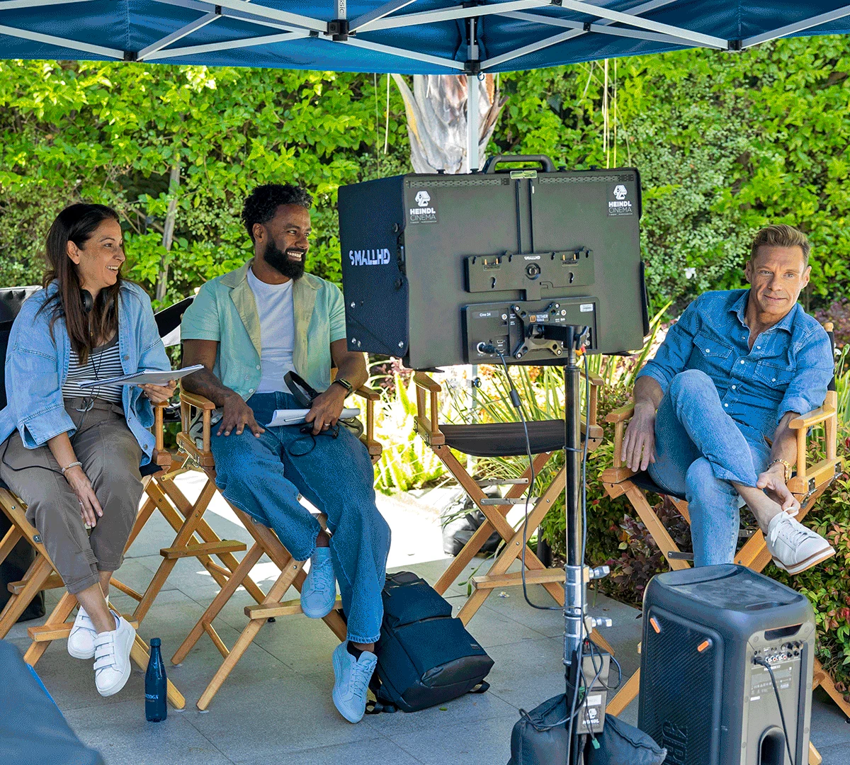 Ryan Seacrest and crew seated beside a production monitor on a patio set in 2026